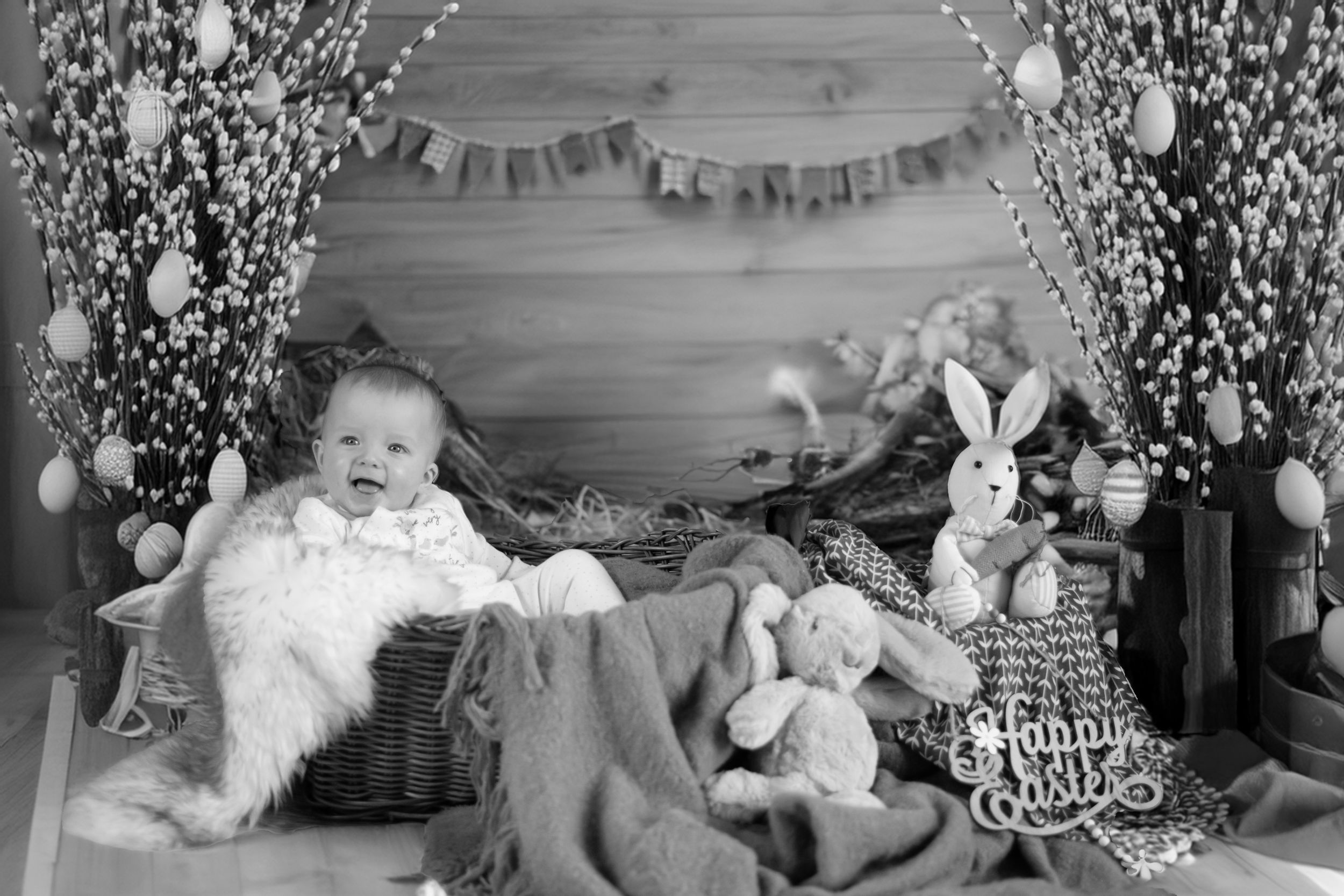Black and white holiday photo setup with stuffed animals, decorations and a wicker basket on rustic wooden backdrop.