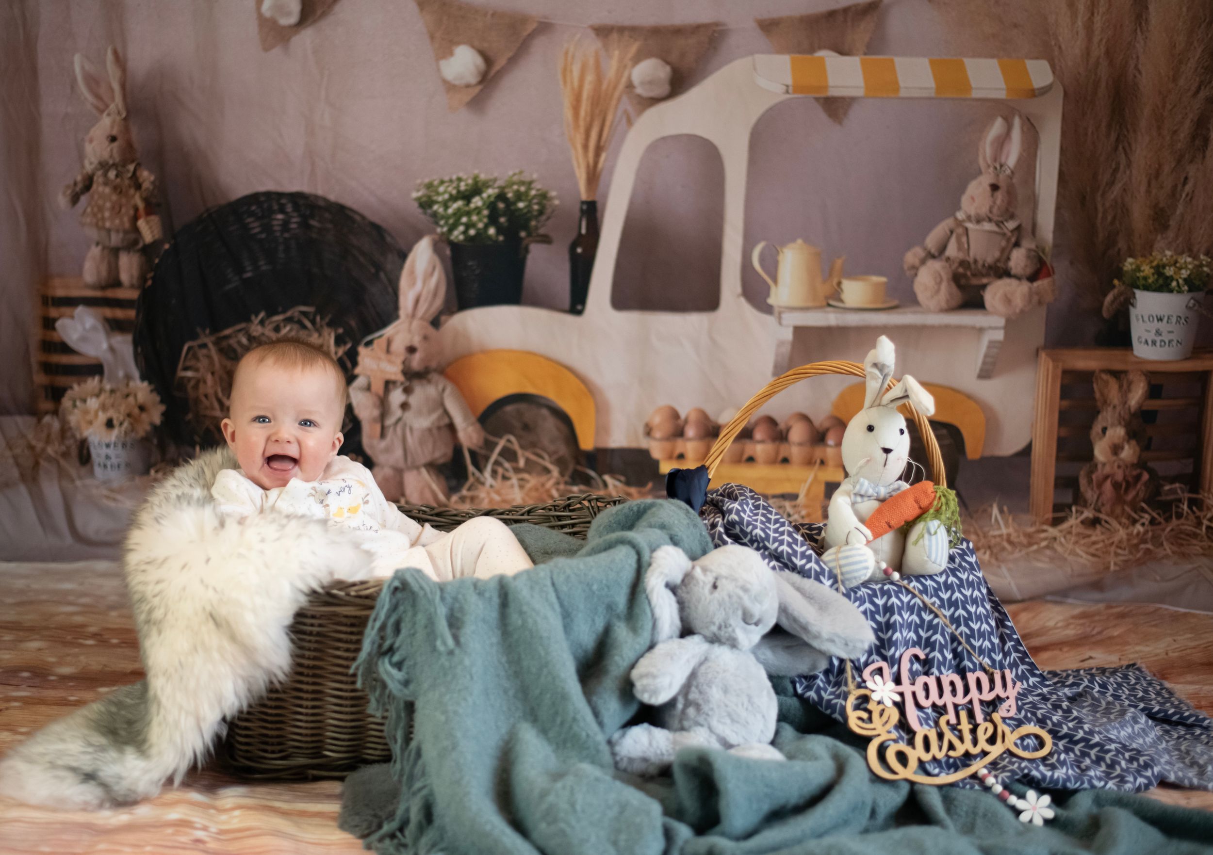 Sweet baby resting in rustic basket with stuffed toys and blankets in vintage-themed studio holiday setting.