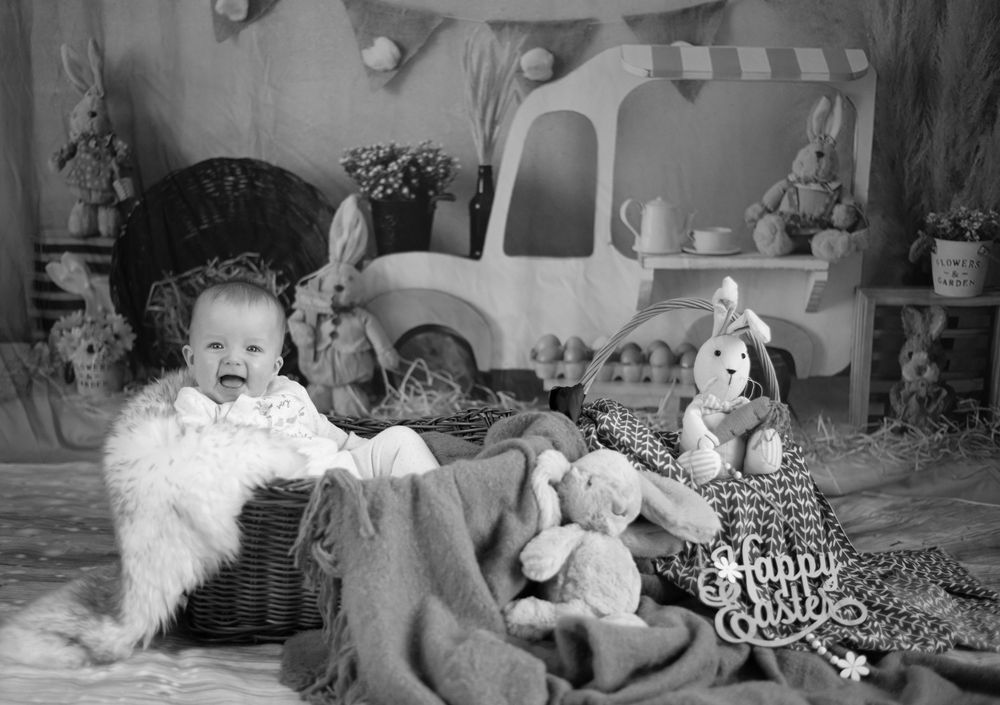 Black and white vintage photo showing a festive holiday scene with toys, stuffed animals and holiday decorations arranged on a floor.