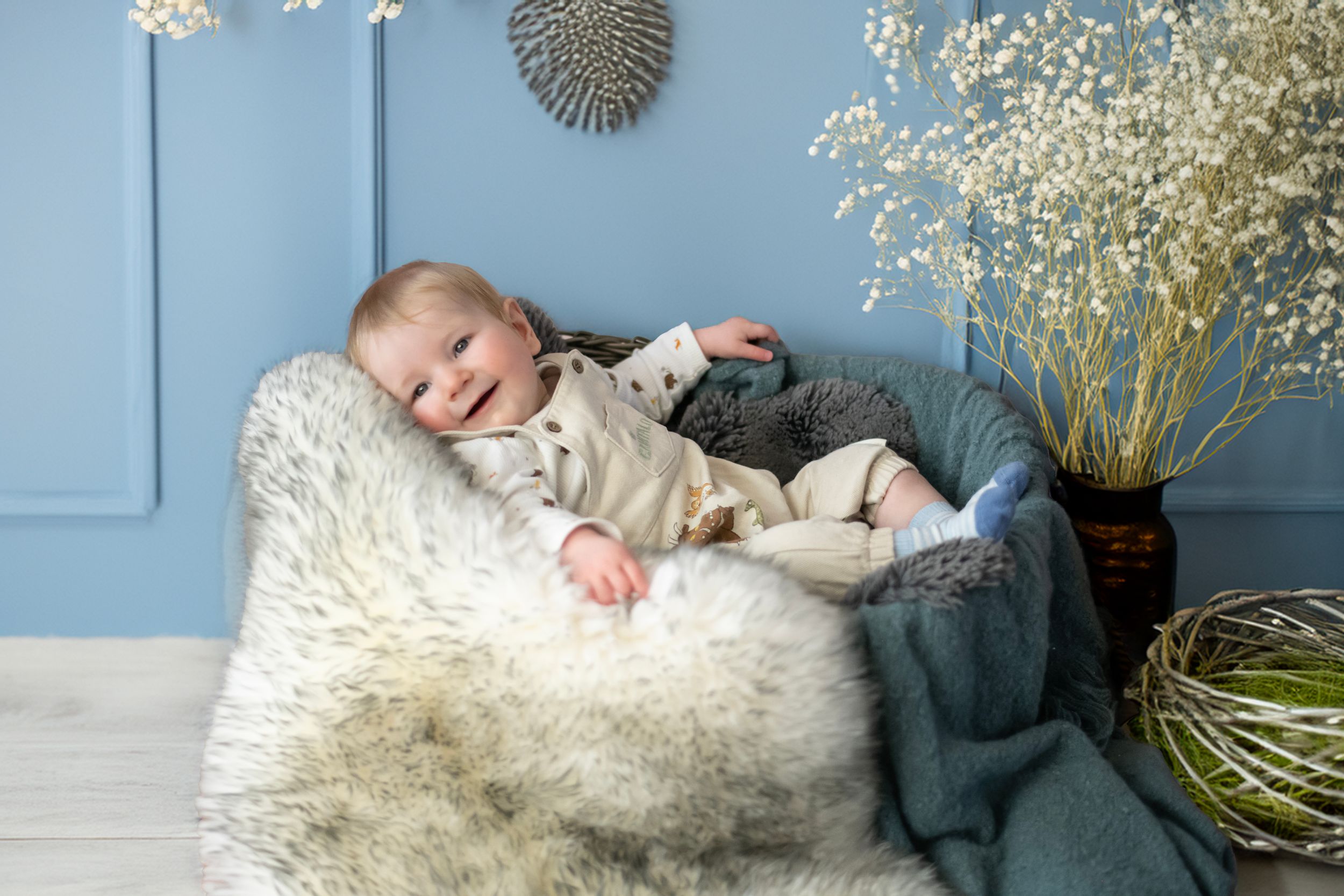 Peaceful infant sleeping on fluffy white fur against blue wall with baby's breath flowers in vase.