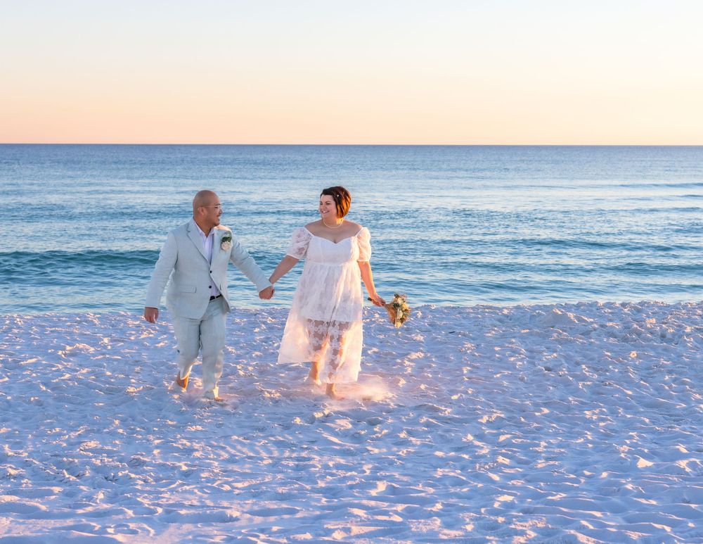 A couple walks hand in hand along a serene beach at sunset with gentle waves in the background.