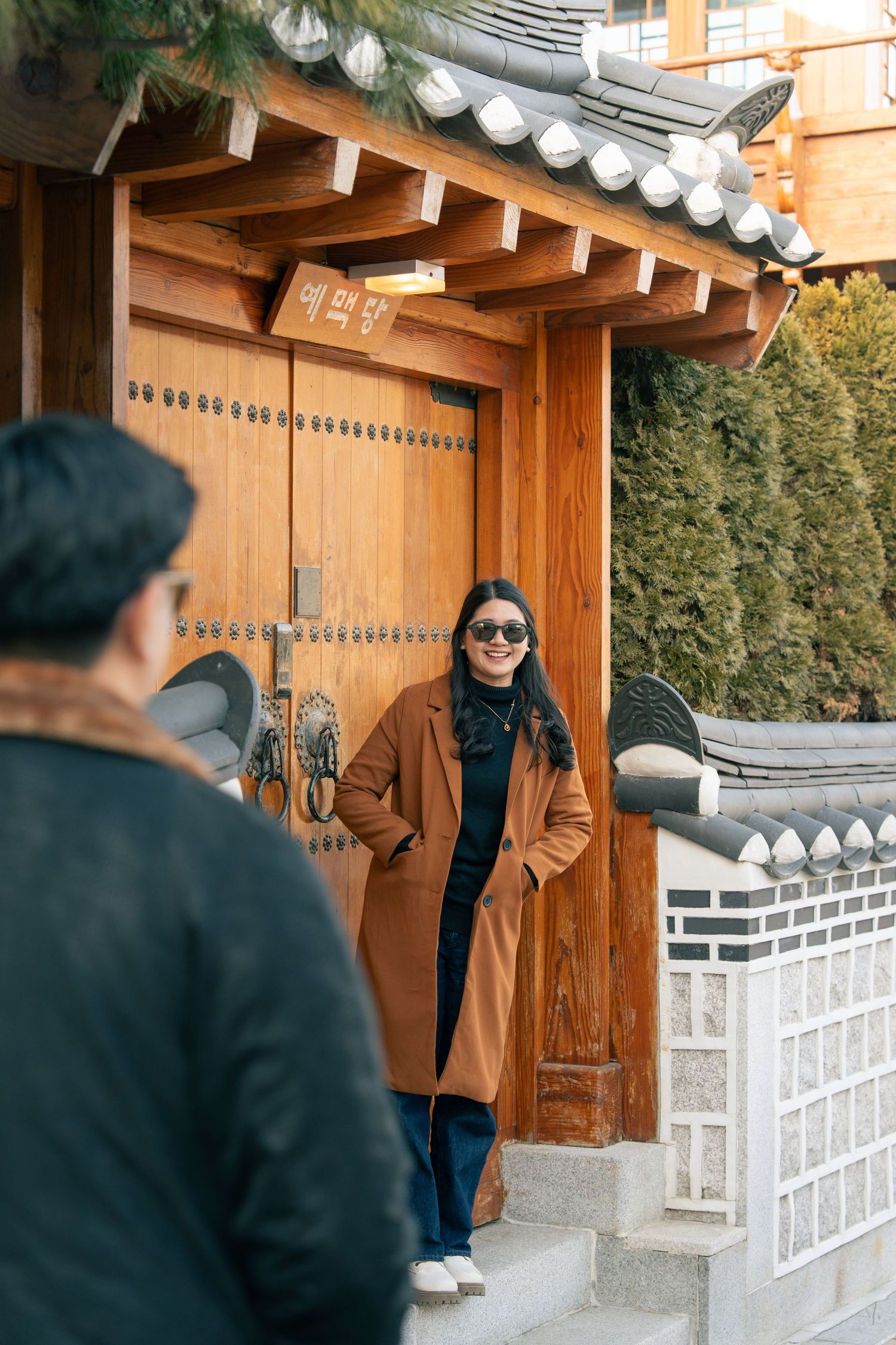 People in traditional Korean hanbok clothing stand near wooden doors and white walls at a historic temple or palace.