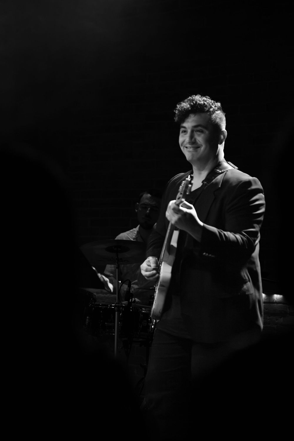 Man smiling while playing an electric guitar on stage.