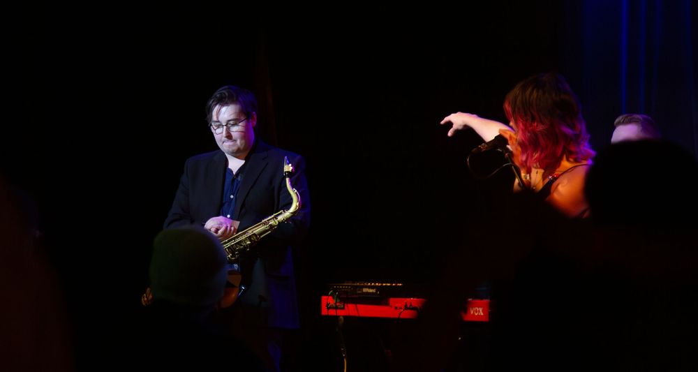 Singer pointing to the saxophone player on stage.