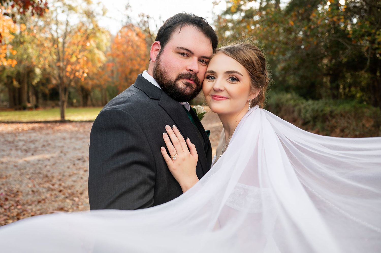 Wedding couple poses together against a backdrop of fall trees and natural light.