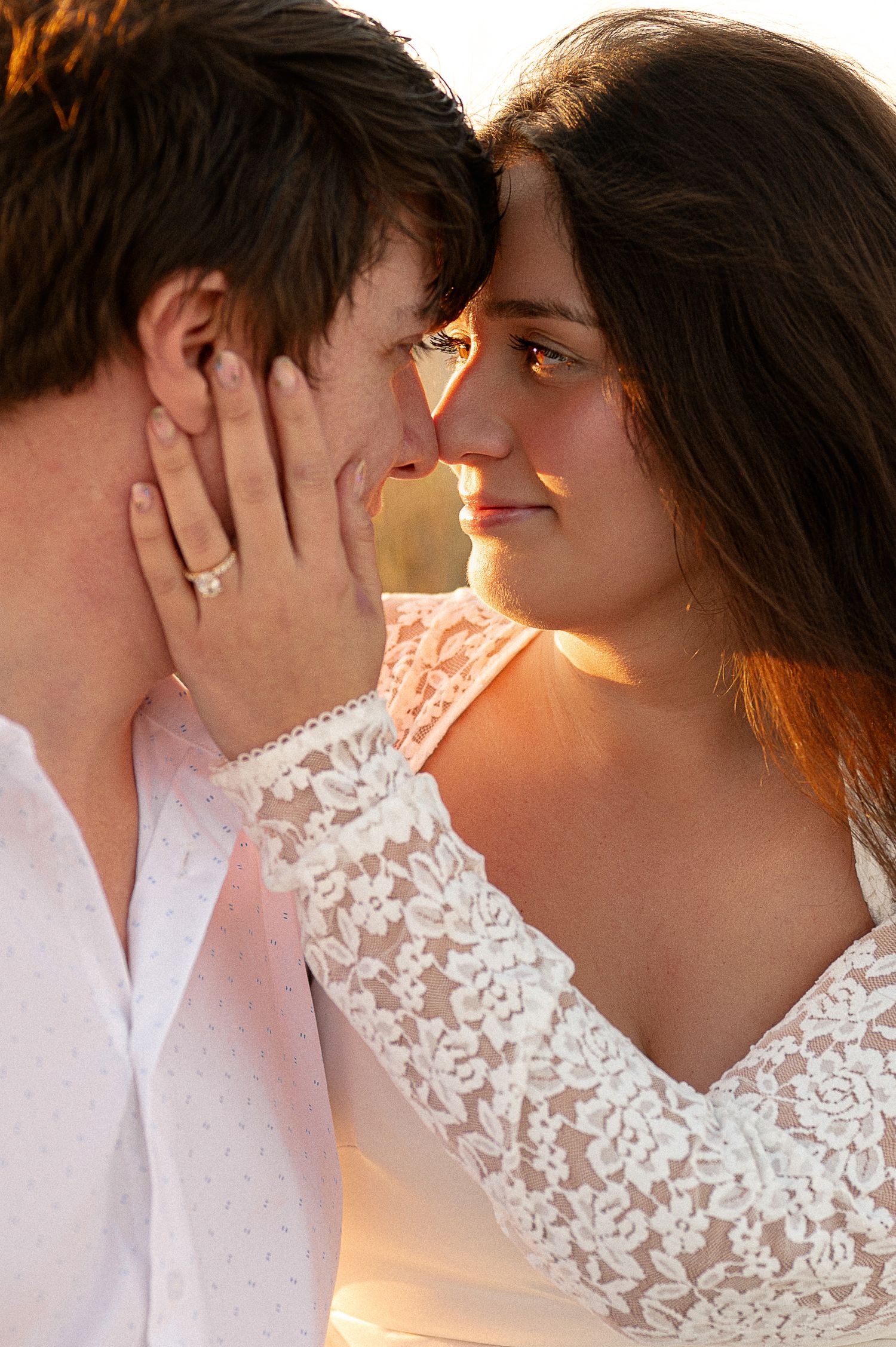 Intimate close-up of couple with woman in lace dress touching partner's face during golden hour.