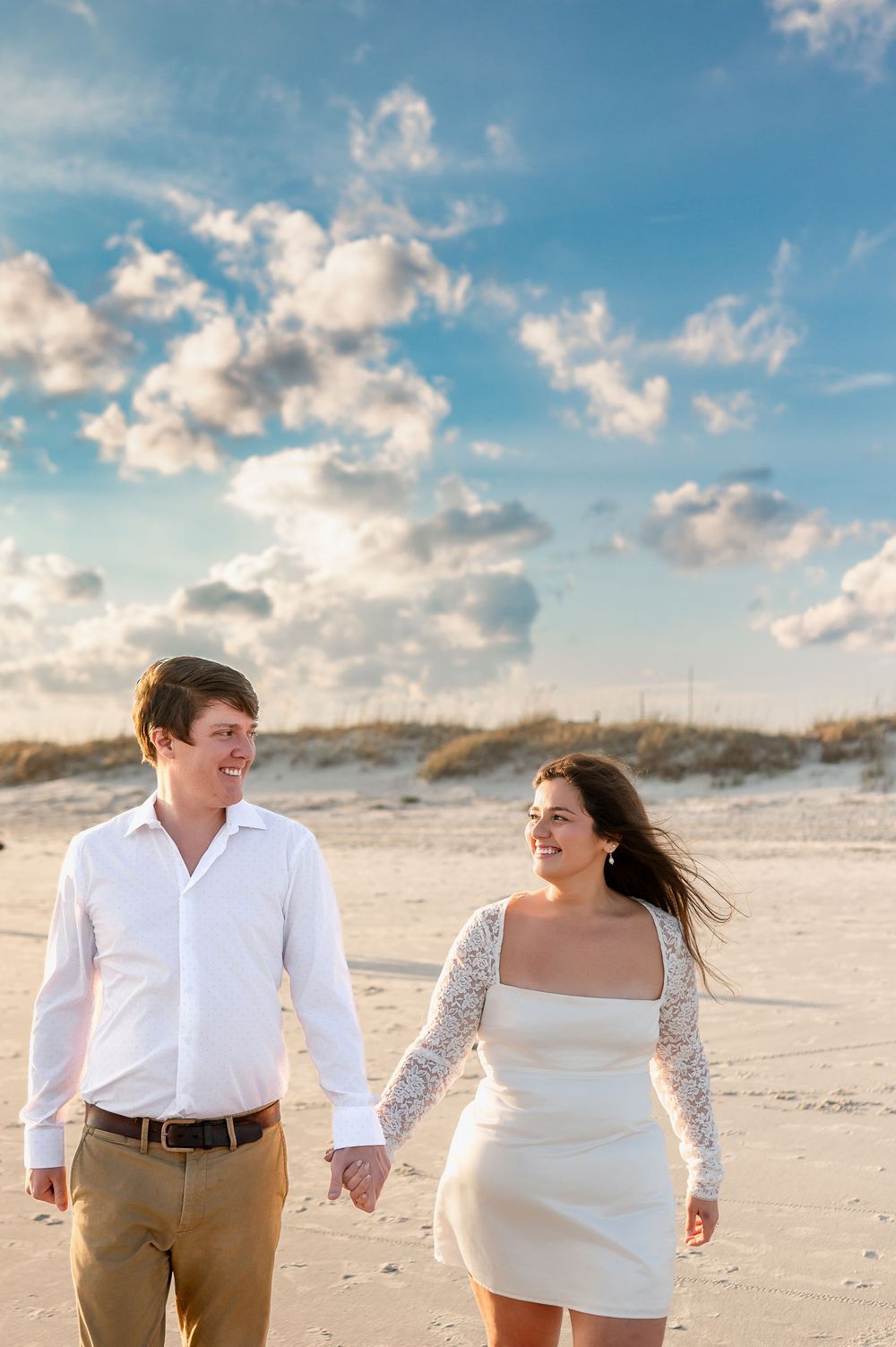 Couple walking and laughing together on sandy beach during golden hour photoshoot.