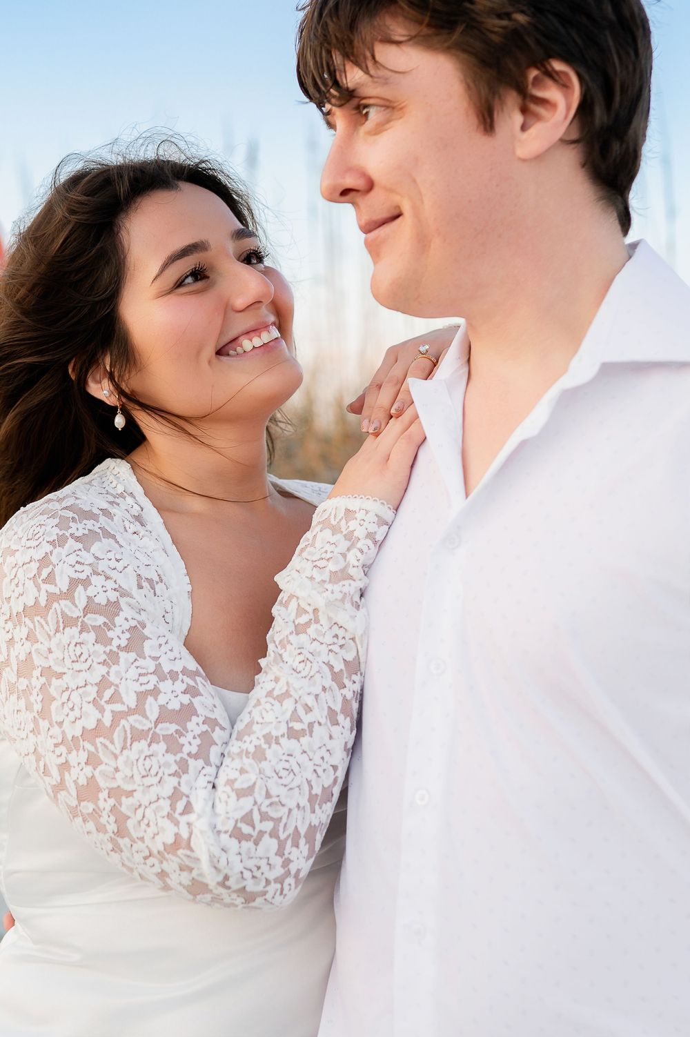 Happy couple in white attire share an intimate moment on a sunny day outdoors.