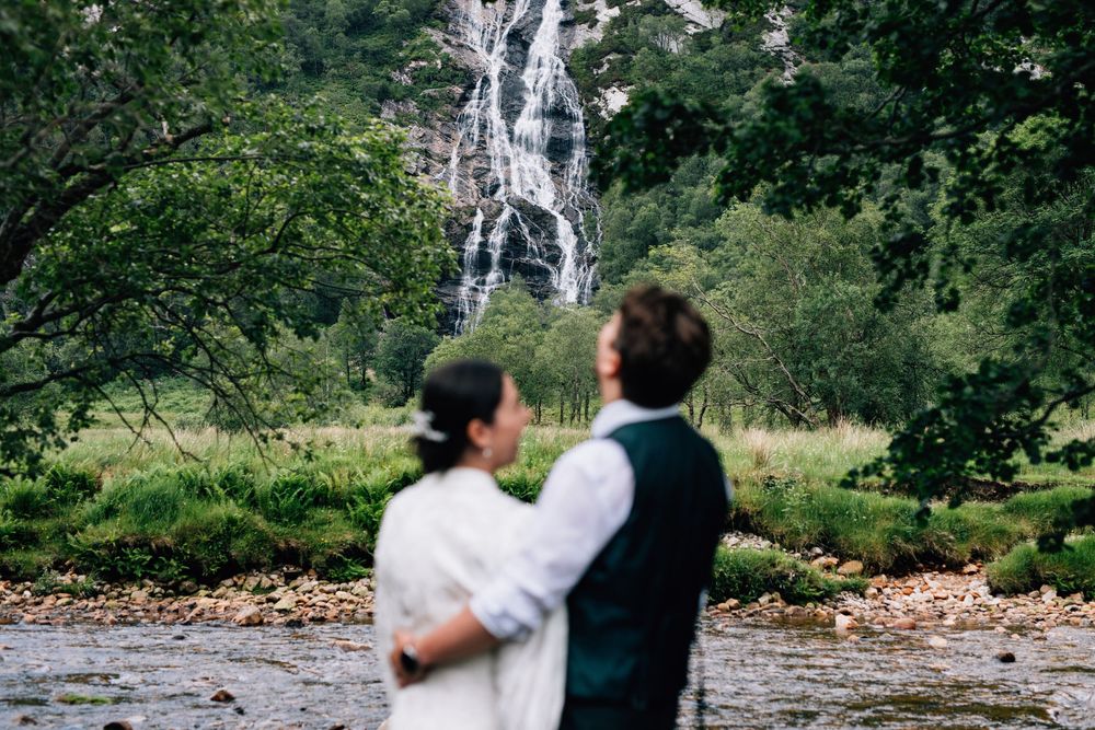 Wedding couple poses in front of a cascading waterfall surrounded by lush greenery.
