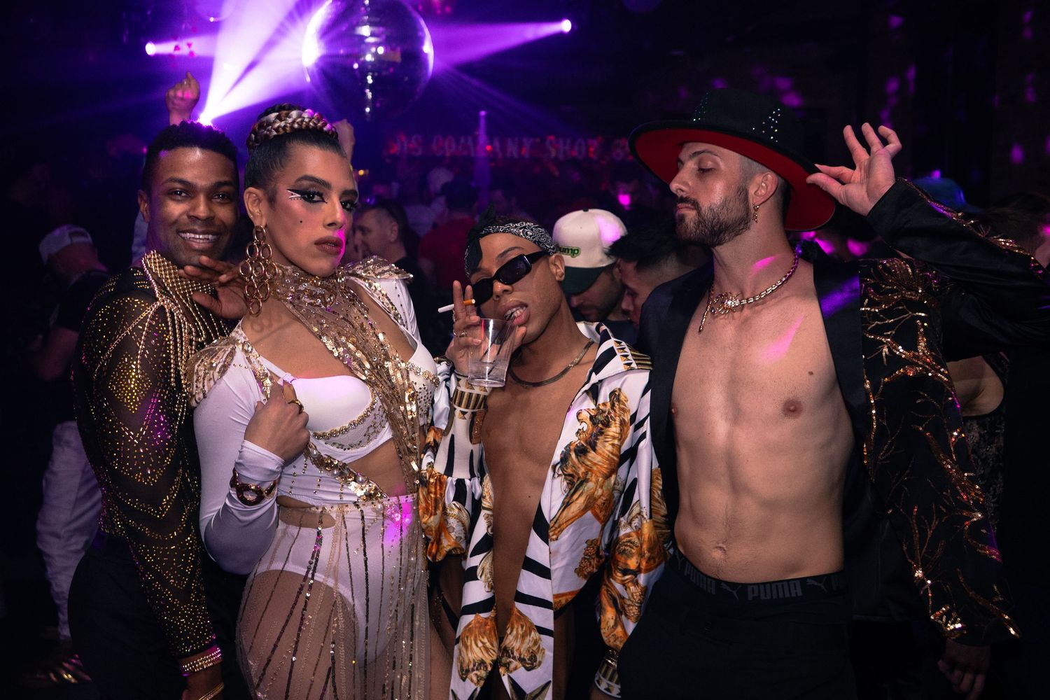 A group of four partygoers post for the camera under purple light with a disco ball in the background at an event in Chicago