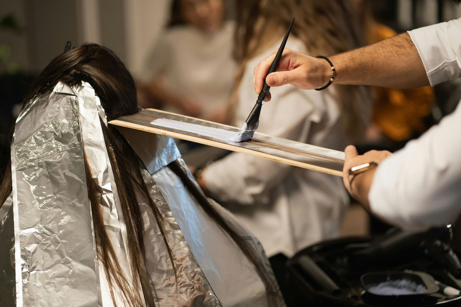 Hair stylist applying foils during a professional blonde hair coloring treatment at salon.