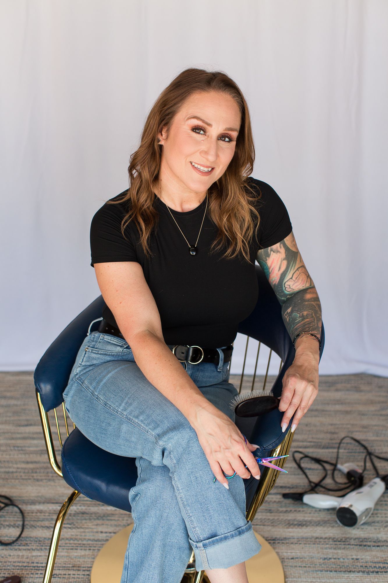Los Angeles Brand Photographer, elevating your business.A person in black t-shirt & jeans sits casually on a chair,with colorful arm tattoos