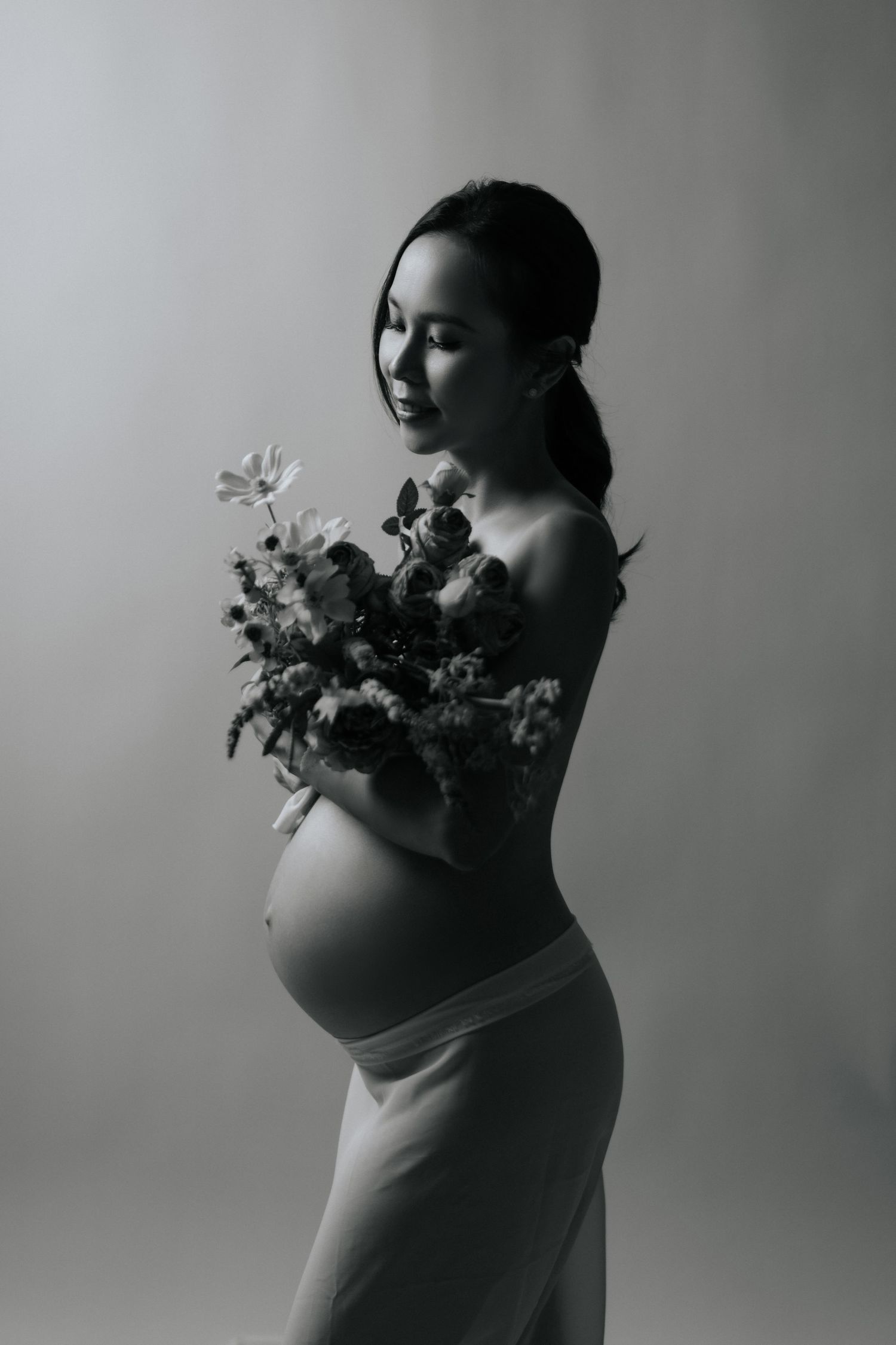 A baby in a floral dress smiles while sitting against a white backdrop with balloons.