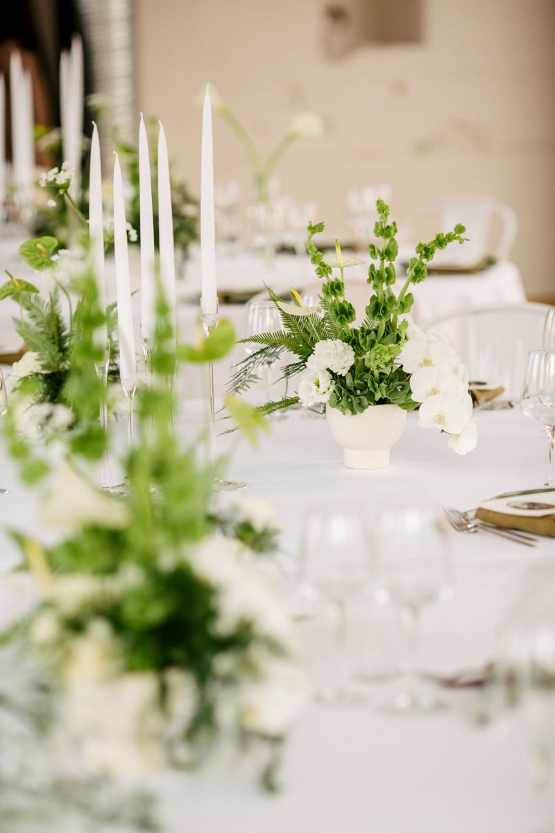 Elegant gedeckter Hochzeitstisch mit grüner Blumendekoration und Kerzen bei einer stilvollen Hochzeitsfeier.