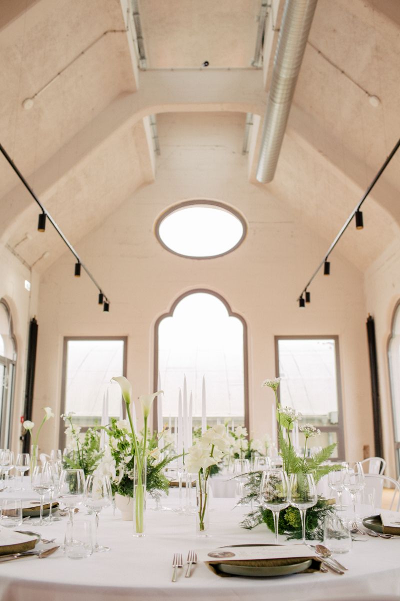 Festlich dekorierter Hochzeitslocation 'die Kathedrale' mit hohen Decken, runden Tischen und eleganter weiss grüner Blumendekoration.