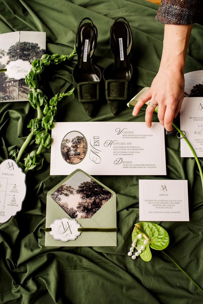 Flatlay Hochzeitskonzept - Hochzeitsdetails mit Einladungskarten, Brautschuhen und floraler Dekoration in Grüntönen.