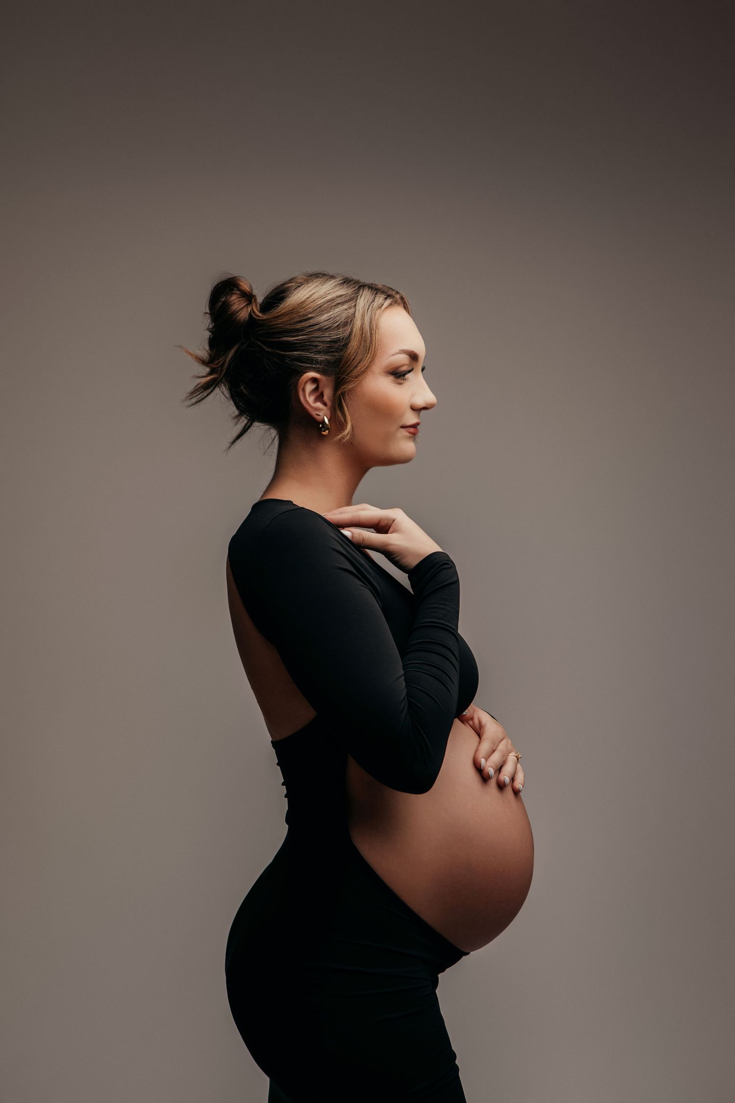 Artistic maternity portraits in black against grey background showing silhouette of pregnant belly.