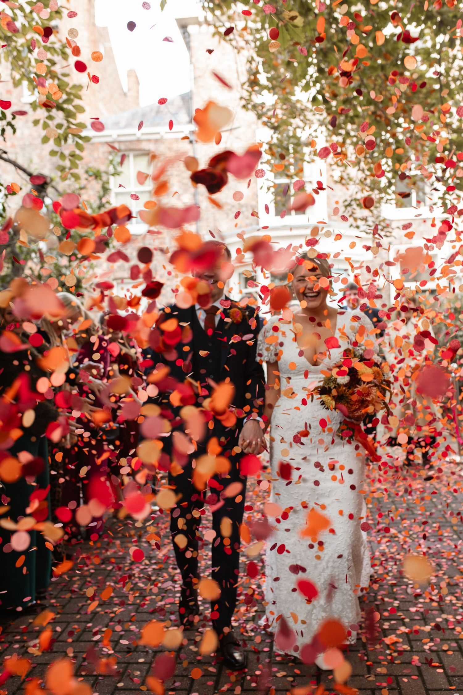 A burst of red and orange confetti fills the air against a brick building backdrop.