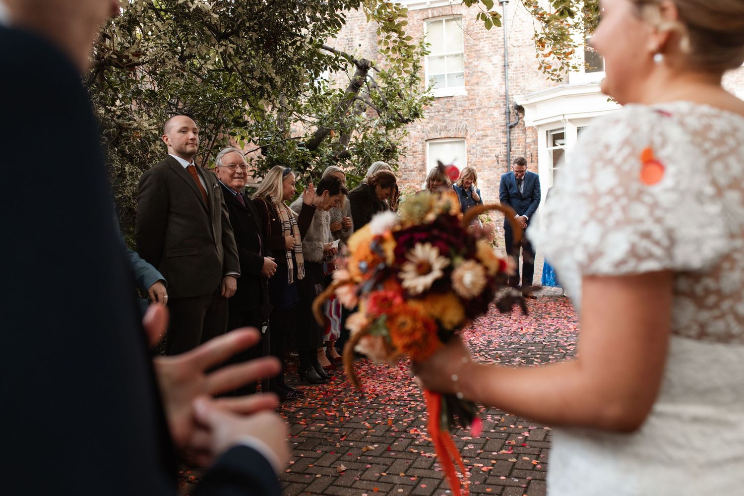 Wedding celebration scene with guests throwing fall foliage and confetti in an outdoor courtyard.