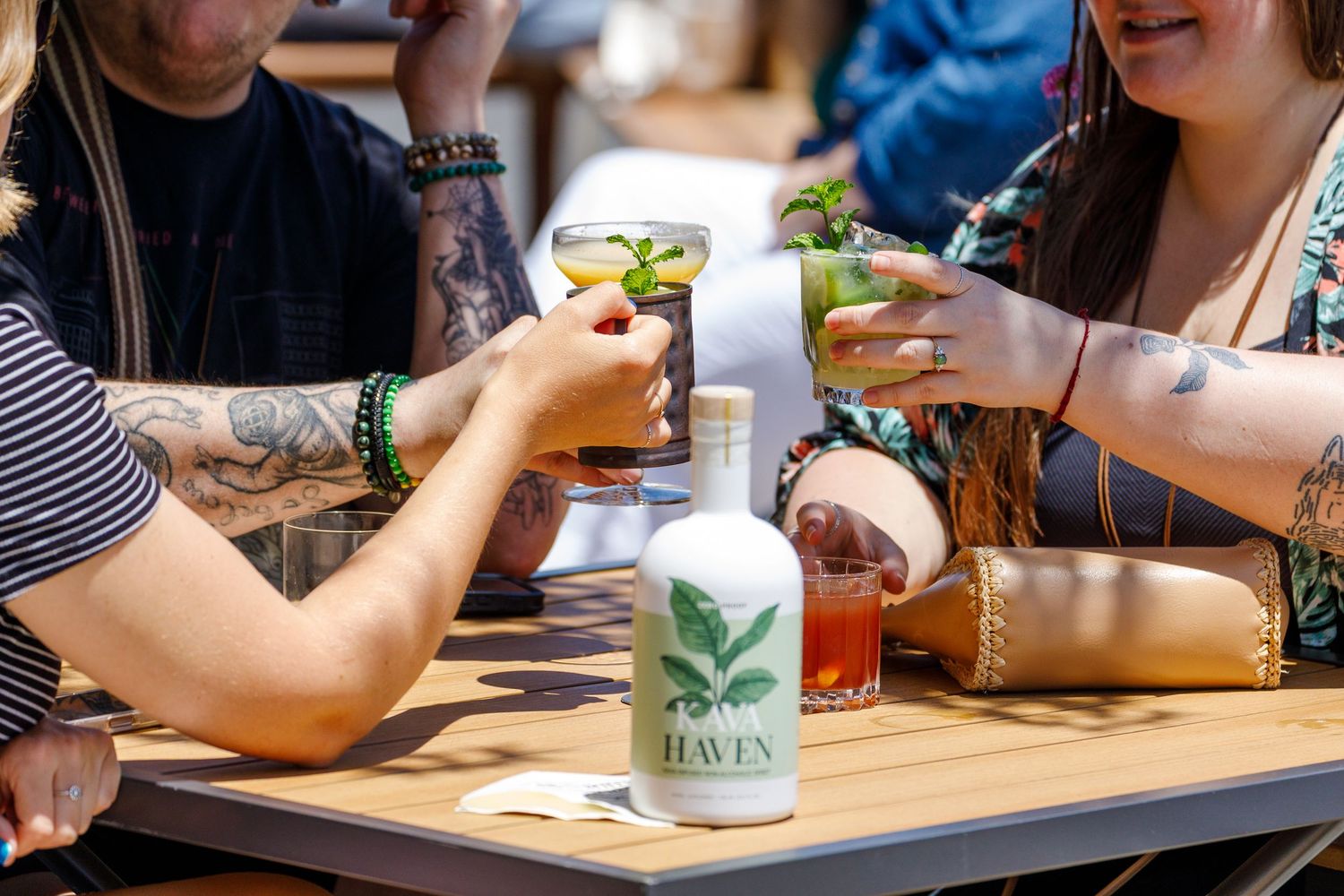 Friends clink glasses with craft beer while enjoying drinks at an outdoor patio table with a bottle of Roots beer.