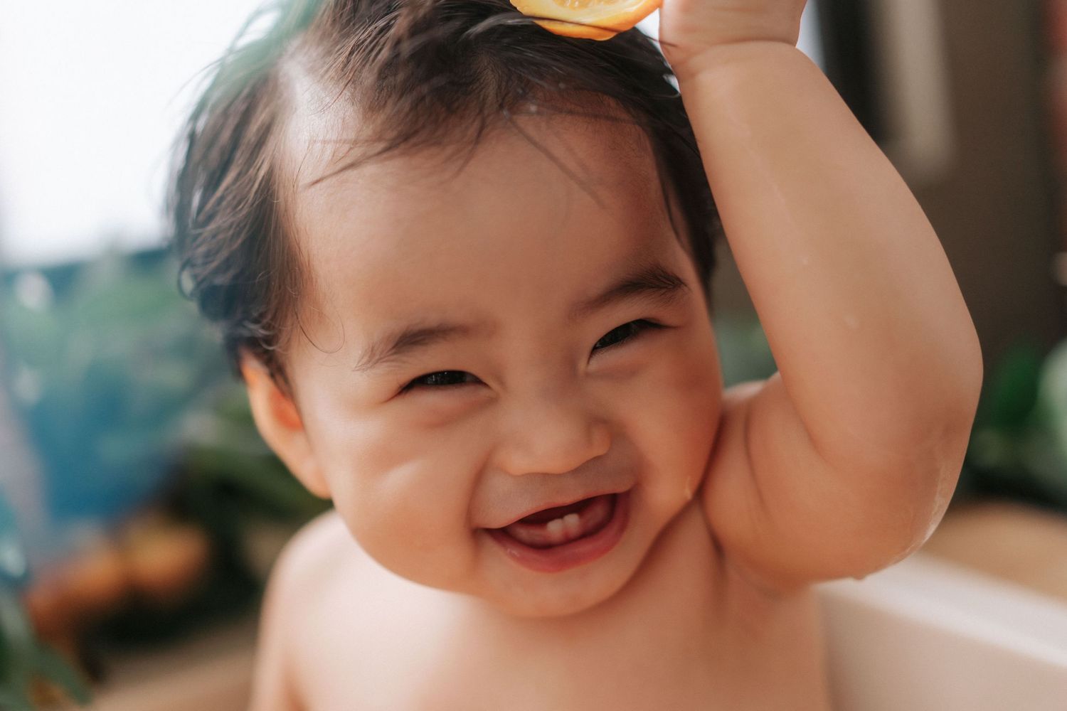 A joyful baby laughs while raising their arm, captured in warm lighting against a soft blurred background.