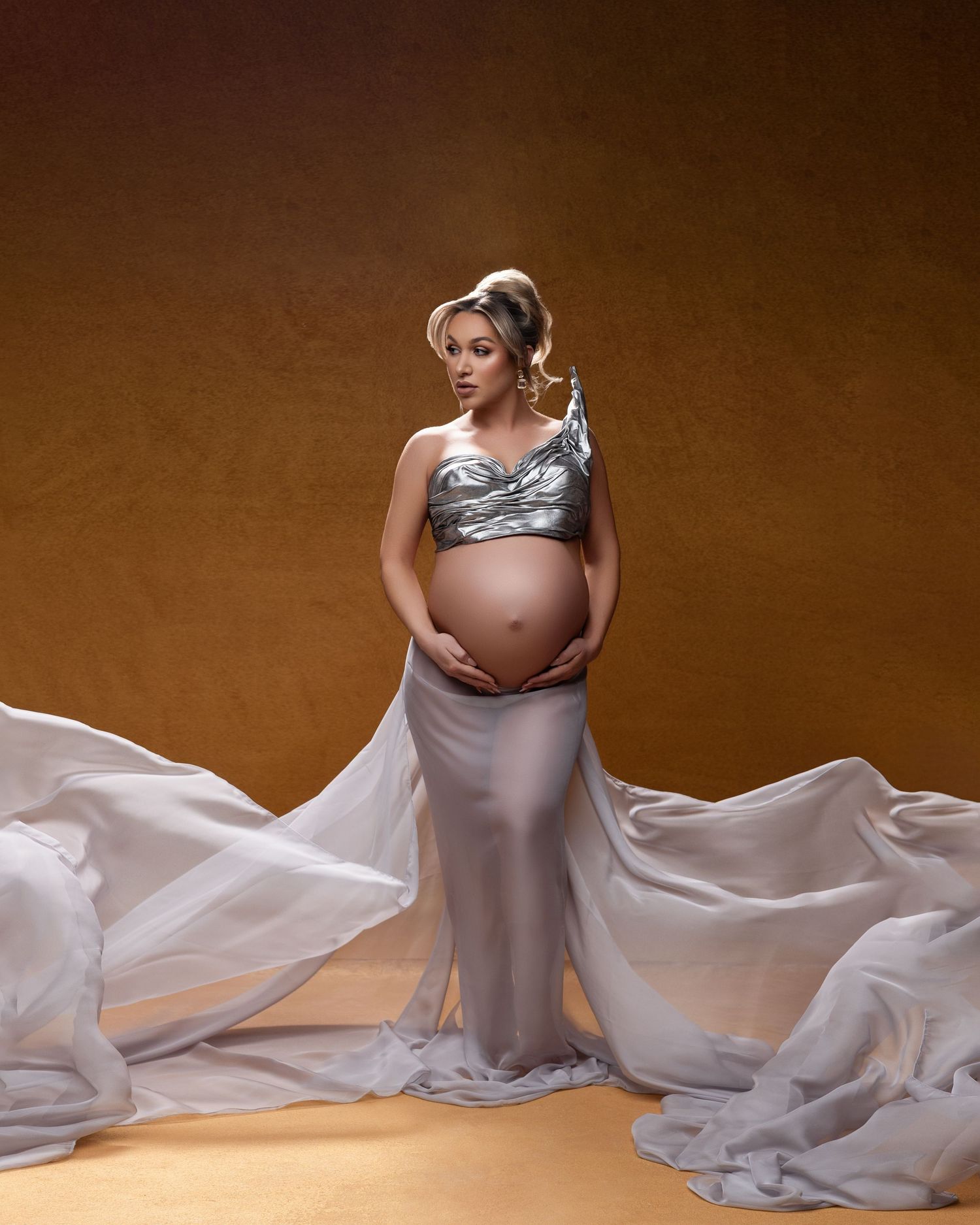 Artistic maternity photo series showing figure in flowing gray fabric against brown backdrop.