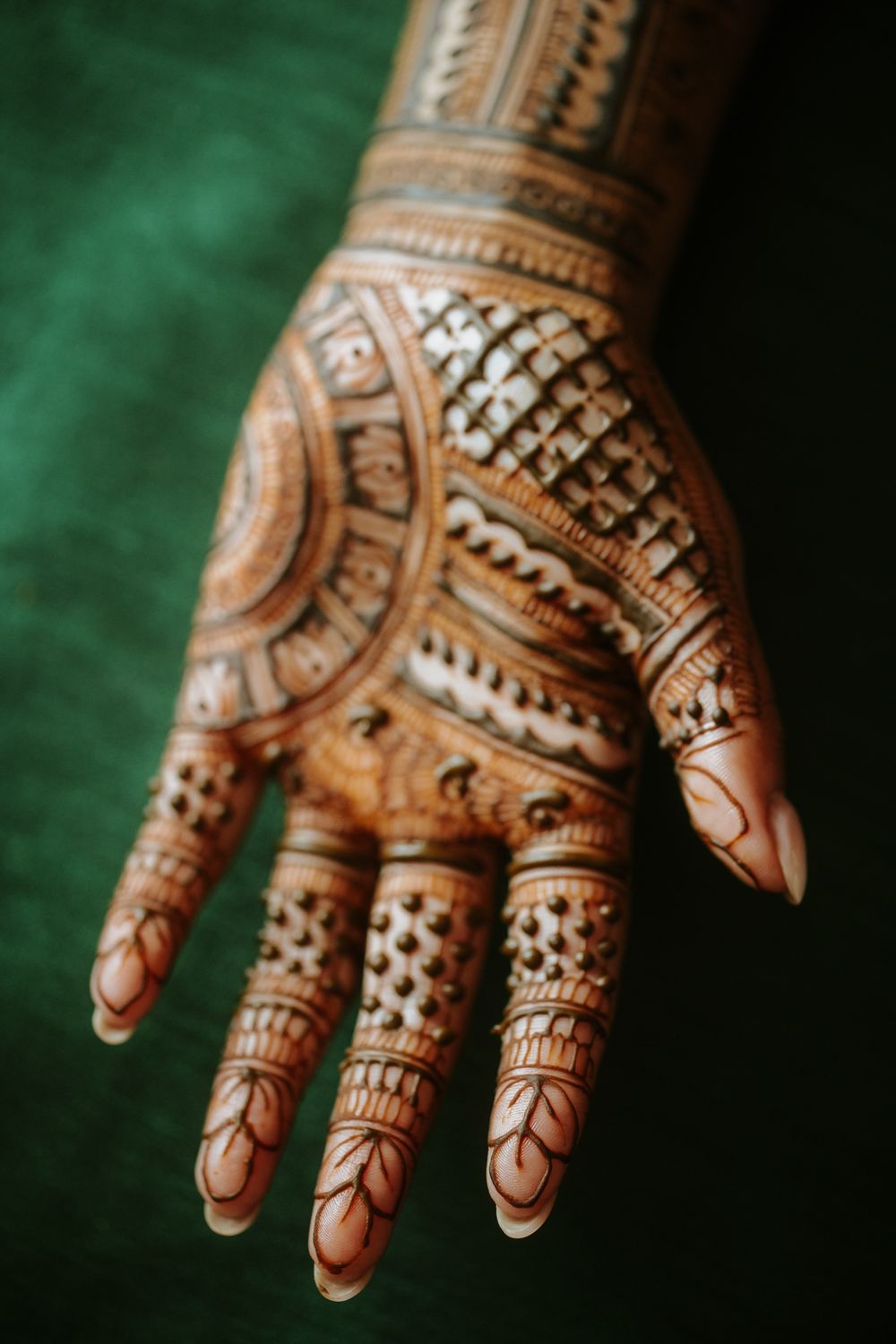 Intricate henna design featuring geometric patterns and floral motifs decorates a palm against a green background.