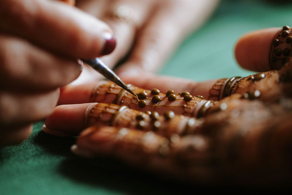 Close-up of hands stringing beads on green fabric showing detailed jewelry making process.