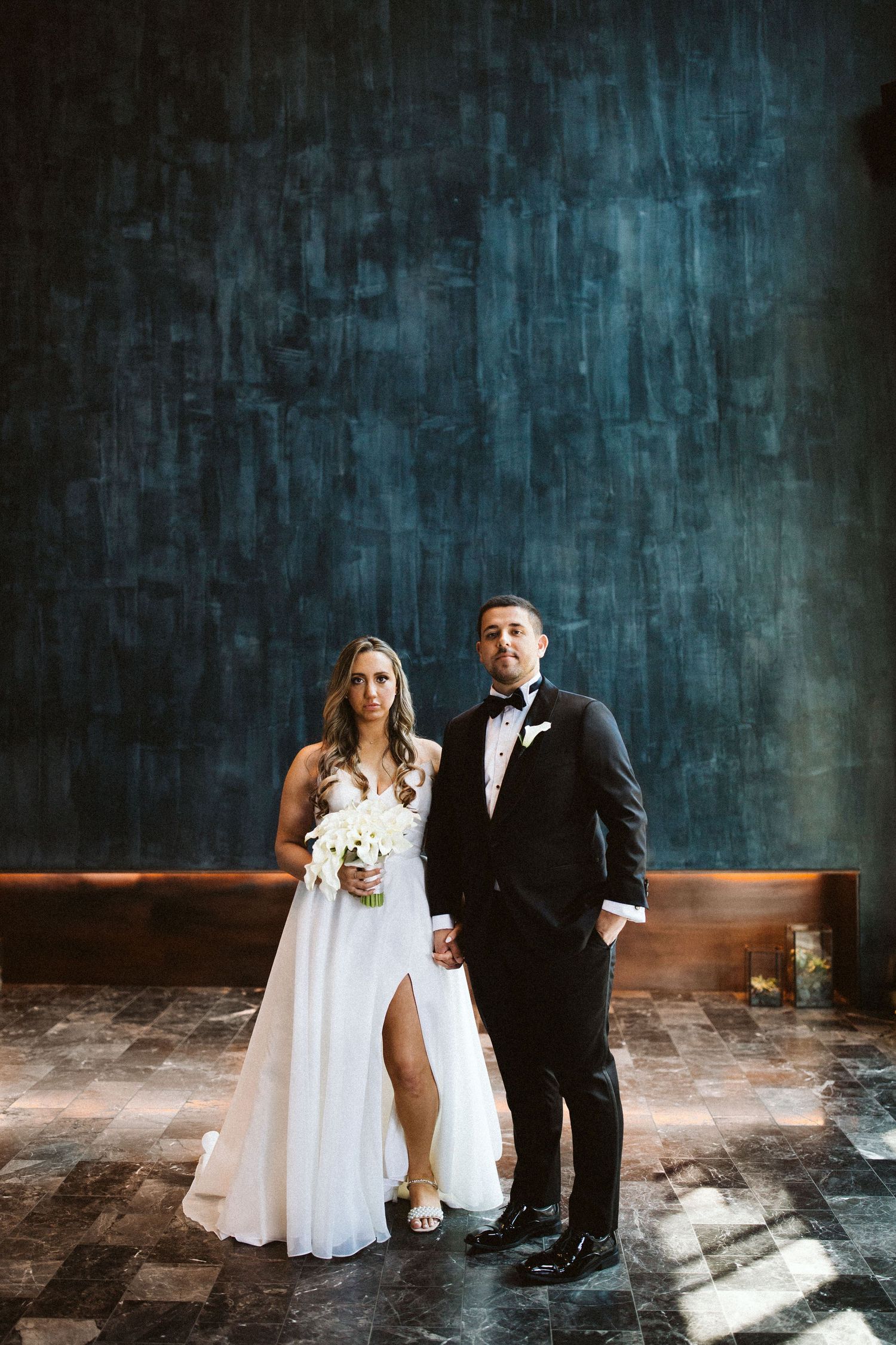 Wedding portraits against textured blue wall with dramatic lighting.