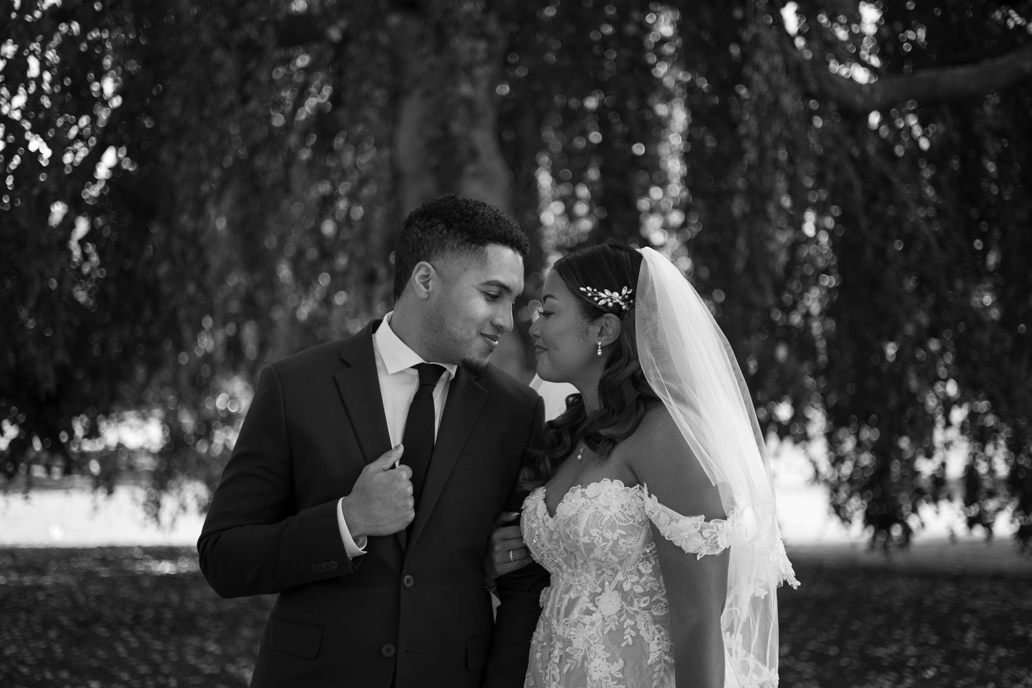 A romantic black and white wedding photo of a couple sharing an intimate moment under willow trees.