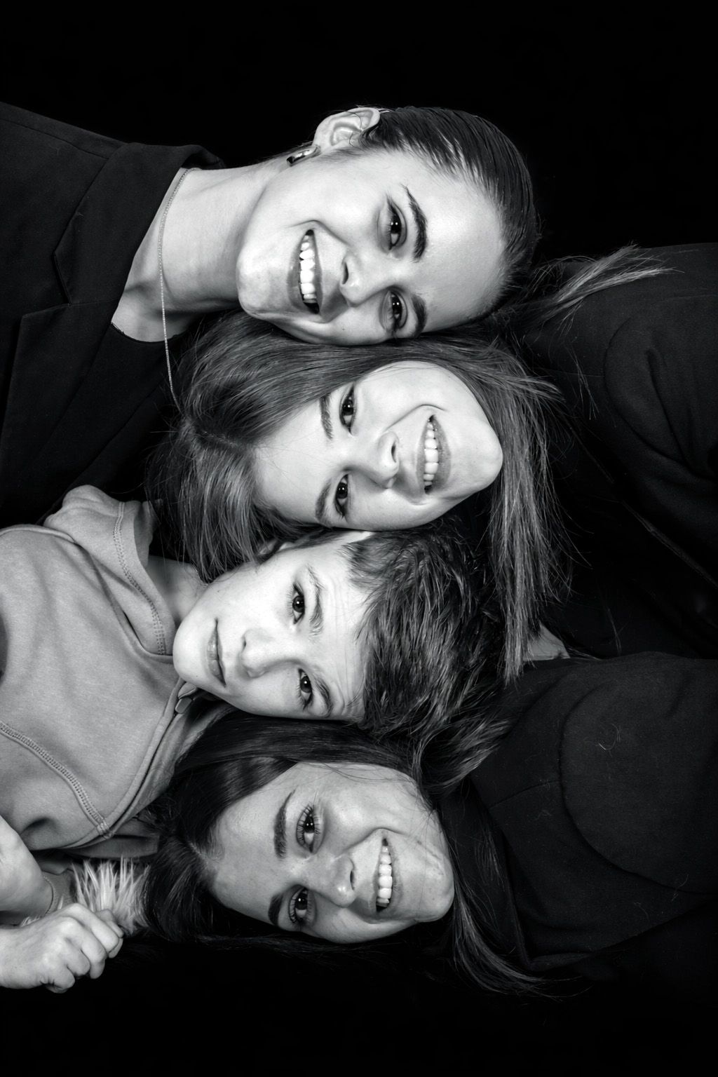 Black and white portrait of four smiling people arranged in a diagonal composition against dark background.