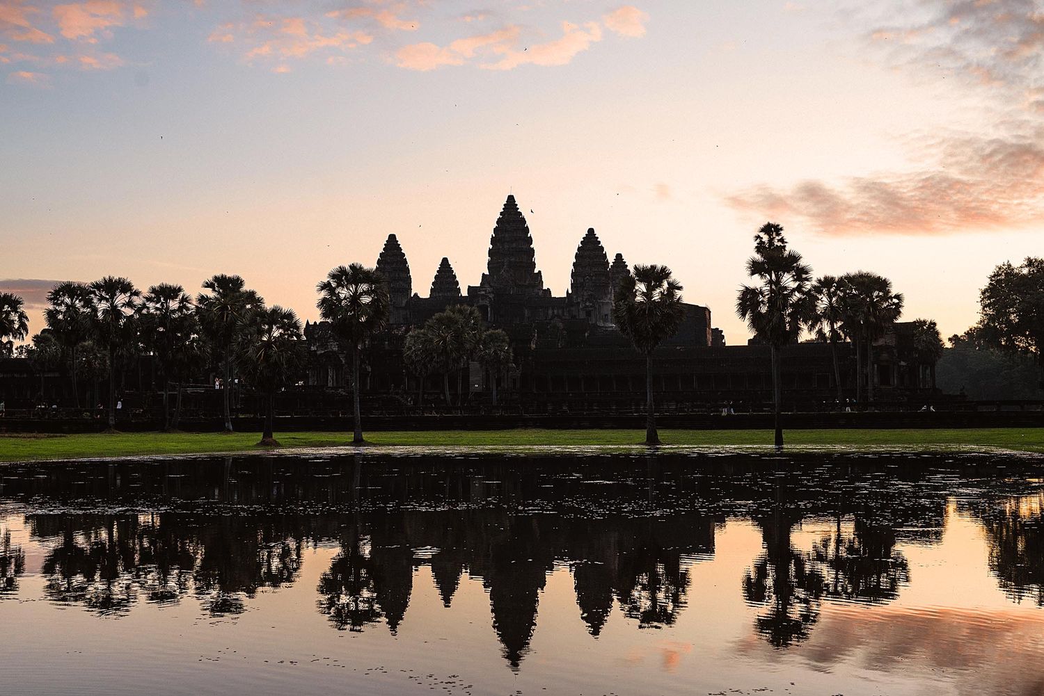 Silhouette of Angkor Wat temple reflecting in still water during dramatic sunset in Cambodia.