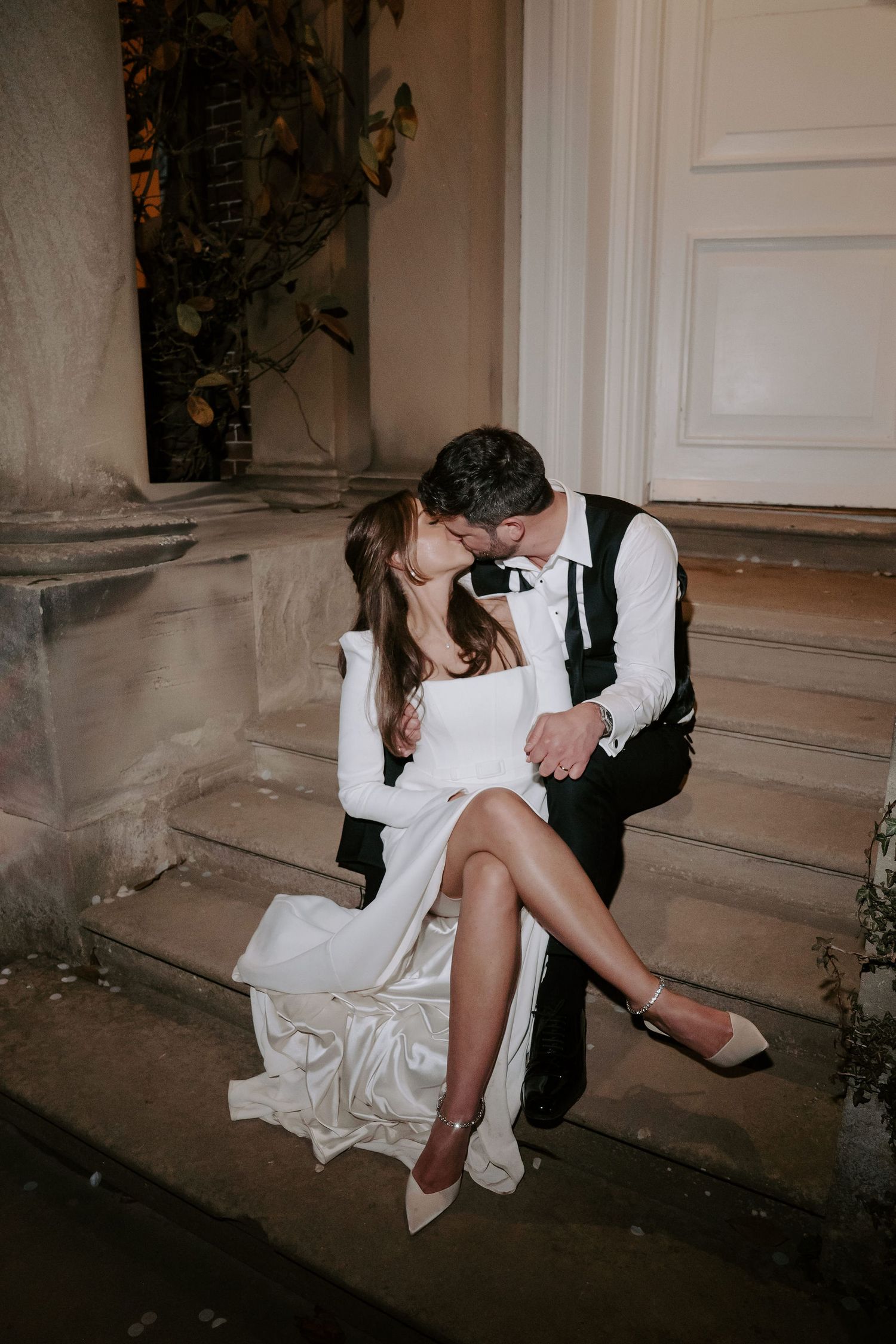 bride and groom kissing sat on steps outside Iscoyd park at night