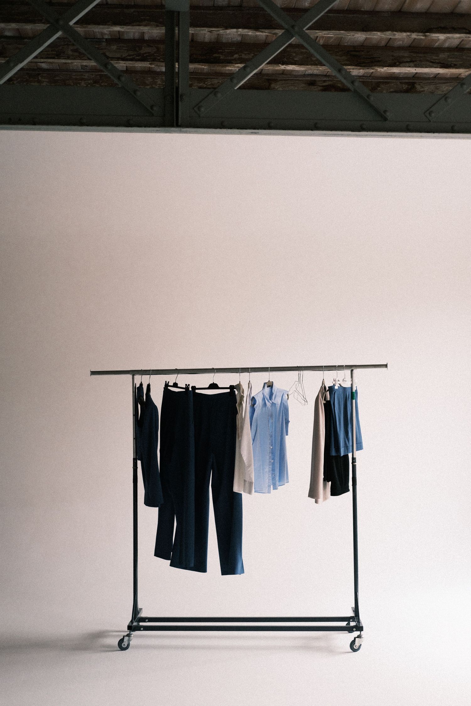 A minimalist clothing rack with blue and black garments hanging against a white wall in an industrial space.