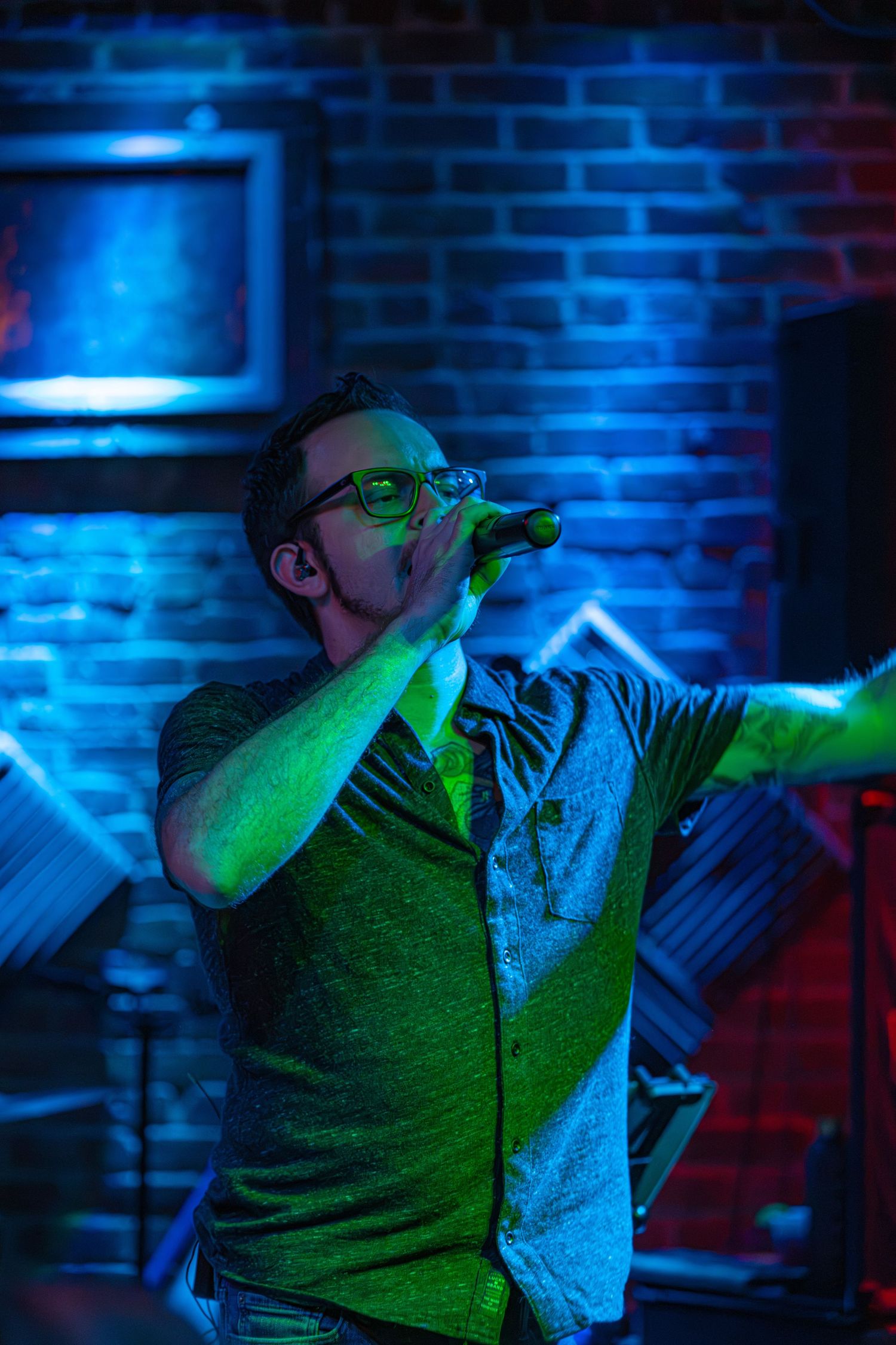 A performer sings passionately on stage bathed in dramatic blue and green lighting at a nightclub venue.