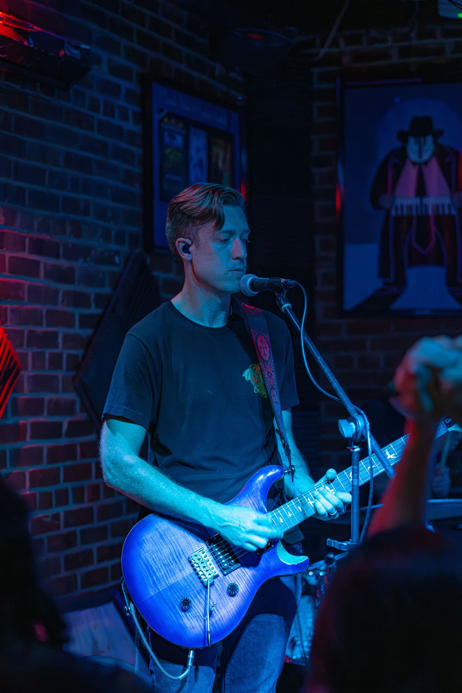 Guitarist performs on stage in dark venue with dramatic blue lighting creating moody atmosphere during live music show.
