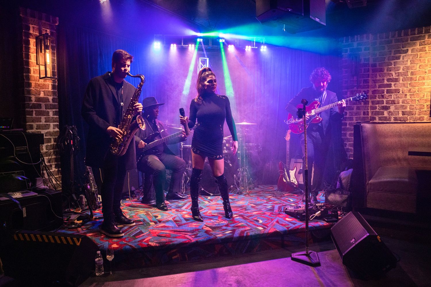 Musicians perform on stage with vibrant purple and blue lighting effects at a live concert venue.