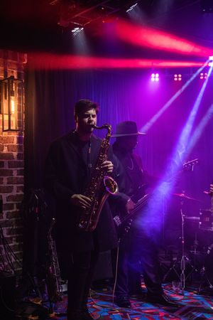 Silhouetted saxophone player performs on stage with dramatic purple and pink lighting effects creating an atmospheric mood.