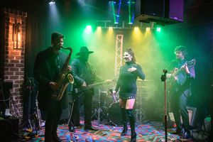 Musicians perform on a dimly lit stage with atmospheric green and blue lighting creating a moody concert ambiance.