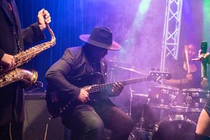 Musicians perform on stage with dramatic blue lighting and fog effects during a live concert performance.