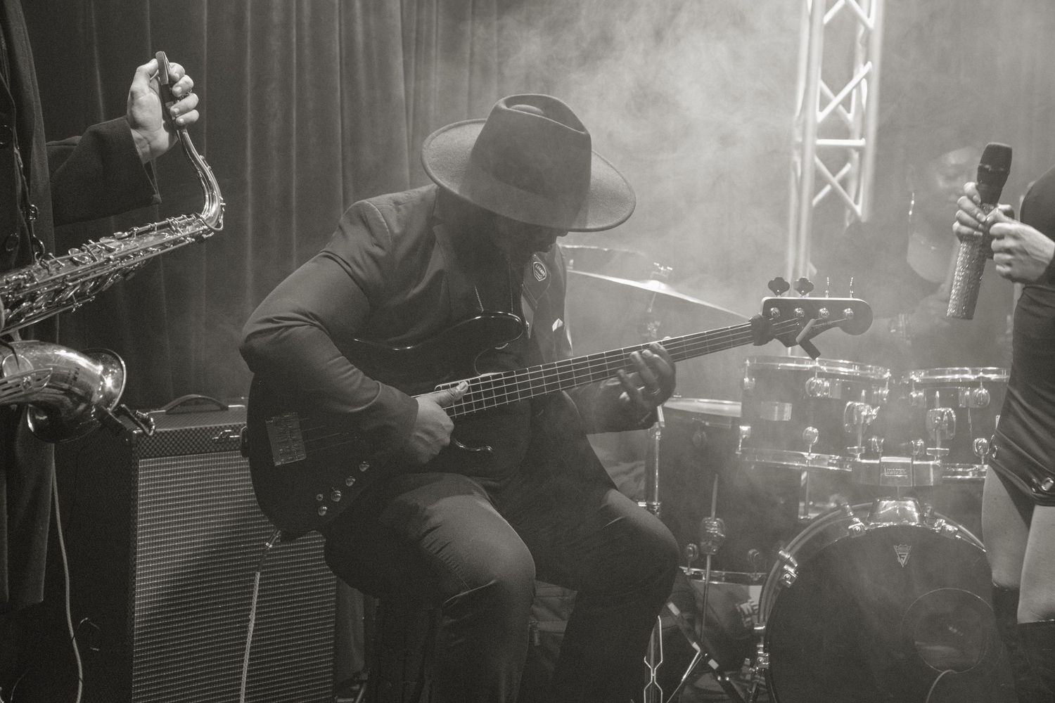 Musicians perform on stage at a live concert venue with dramatic lighting and multiple instruments visible.
