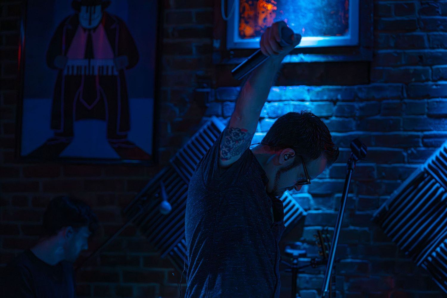 A silhouetted figure performs against a moody blue-lit brick wall backdrop in a dimly lit venue.