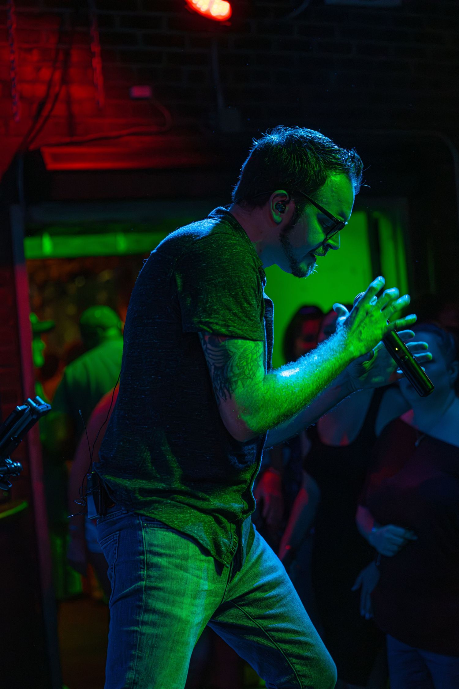 A performer singing into a microphone on stage under dramatic blue and green lighting during a live show.