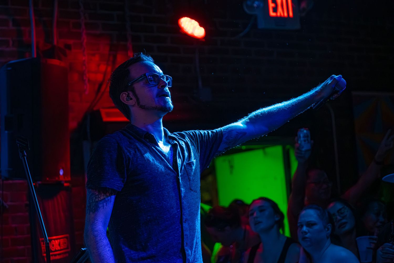 A person performs on stage in a dark venue with dramatic red and blue lighting effects.