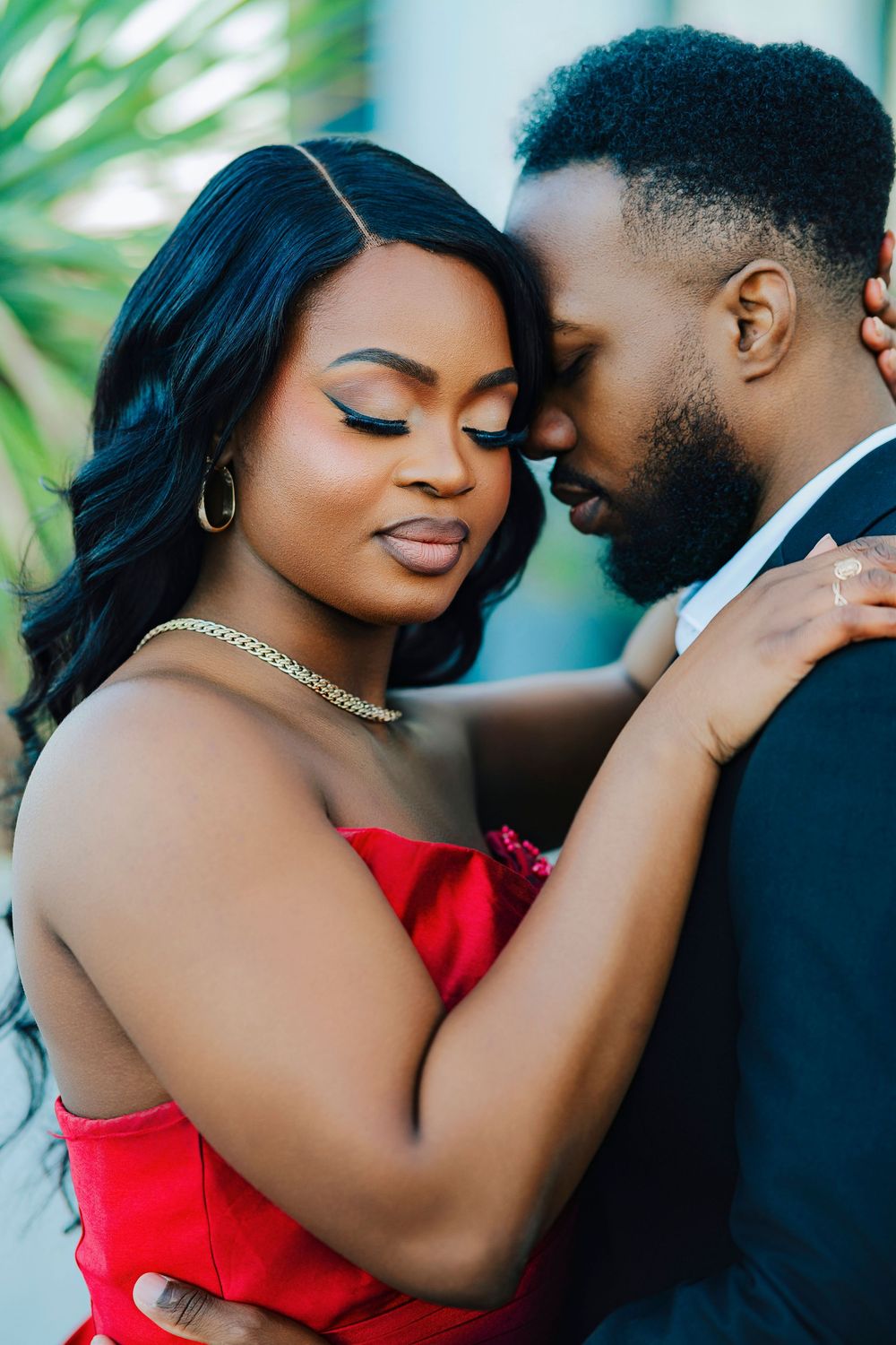 A romantic couple embraces while wearing formal attire against a tropical backdrop.