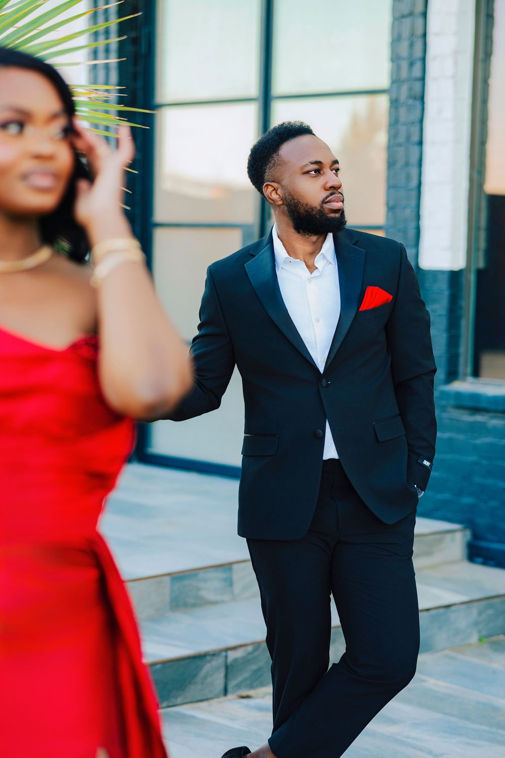 A couple poses for engagement photos in formal attire, with the person in red and the other in a black suit.