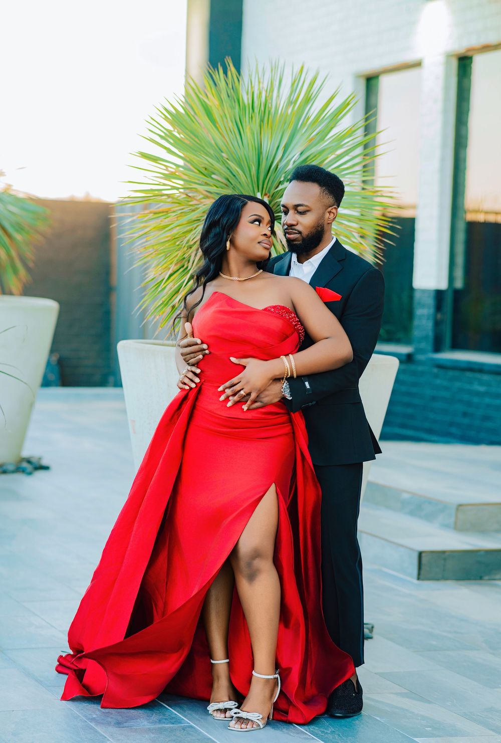 A couple shares an intimate moment while dressed in red and black formal wear.