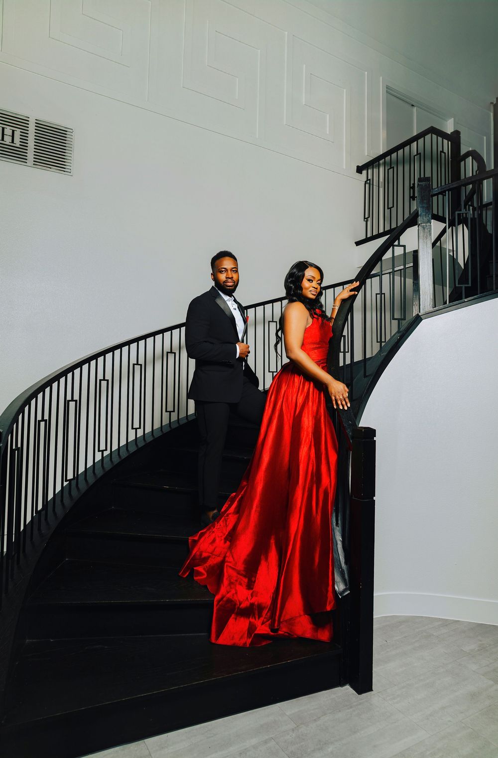 A couple in formal wear ascends a modern staircase as the red dress creates dramatic movement.