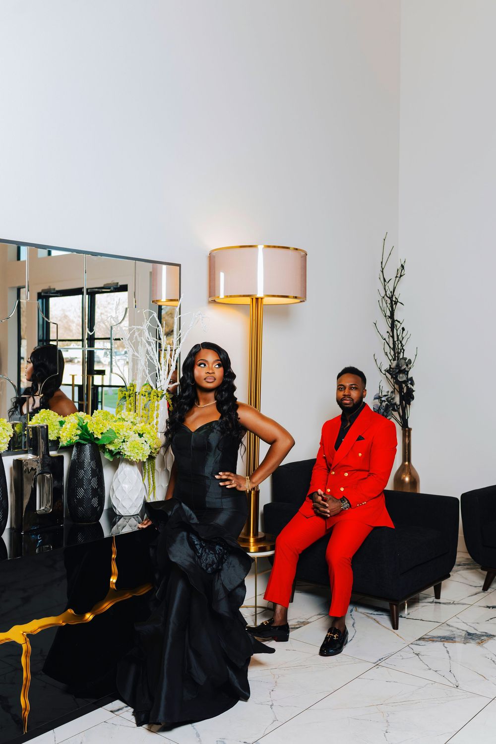 Elegant indoor photoshoot featuring couple in red and black formal attire against white modern decor.