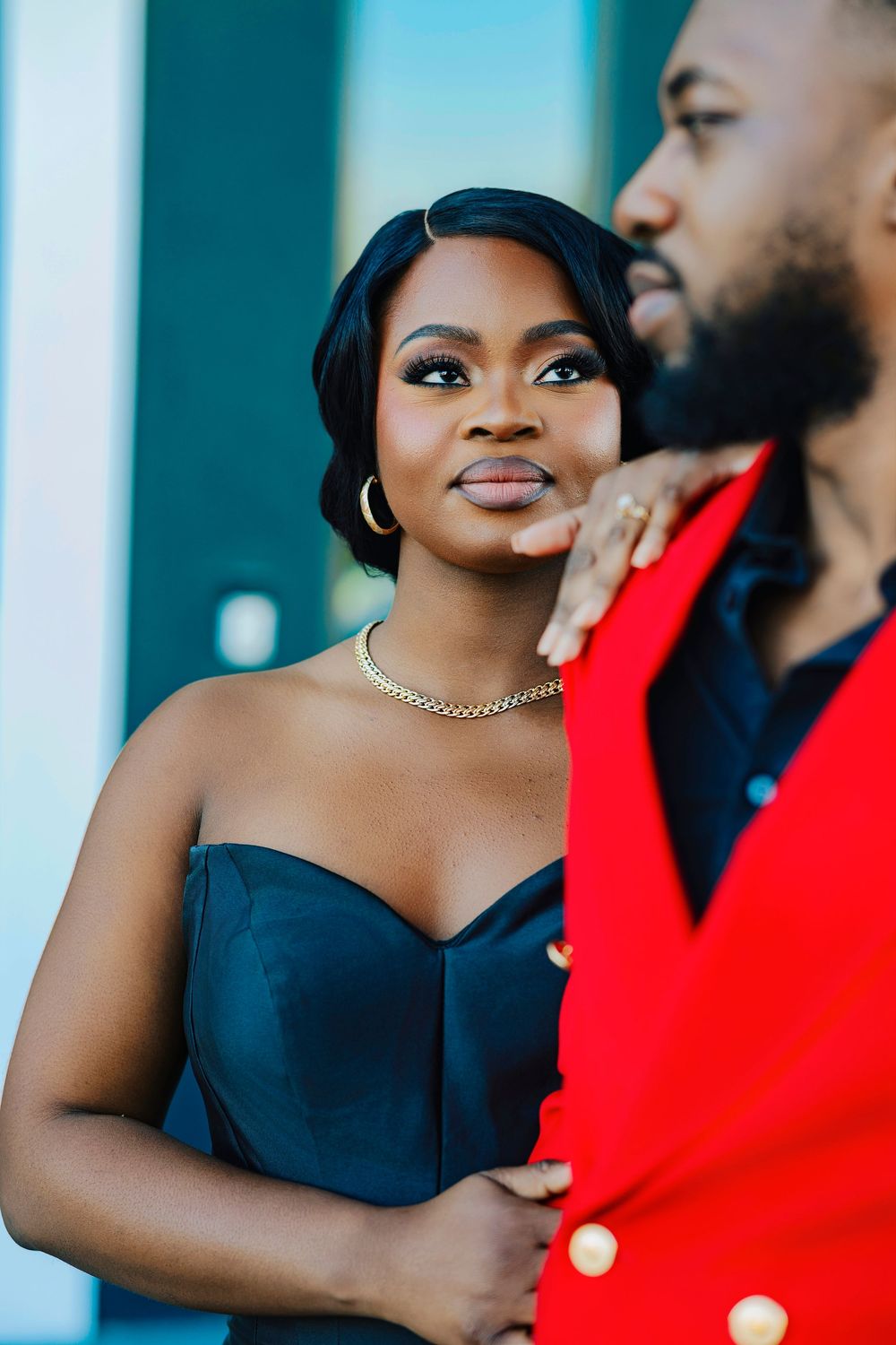 A close-up portrait shows a couple in formal wear, with a black dress and red blazer against a teal background.